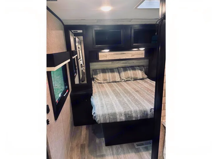 RV rental bedroom interior with a striped bed, overhead storage, and a mirror. Comfortable sleeping area.. Jayco Jay Feather 2022