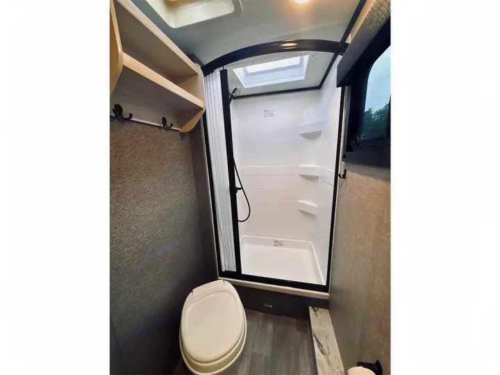 Clean RV rental bathroom with a white toilet, standing shower, skylight, and upper shelves for storage.. Jayco Jay Feather 2022