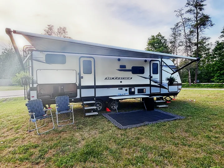 This Jay Feather RV rental is ready for adventure: travel trailer campsite with extended awning, outdoor kitchen, and chairs on green grass.. Jayco Jay Feather 2022