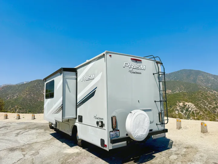 White 'Prism Coachmen' RV rental parked at a mountain overlook under a clear blue sky, ideal for outdoor travel.. Coachmen RV Prism Select 24CB 2021