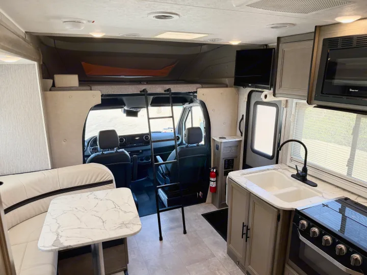 Spacious RV rental interior: dinette, full kitchen with sink and stove, overhead bunk, and front cab view. Perfect for adventures.. Coachmen RV Prism Select 24CB 2021