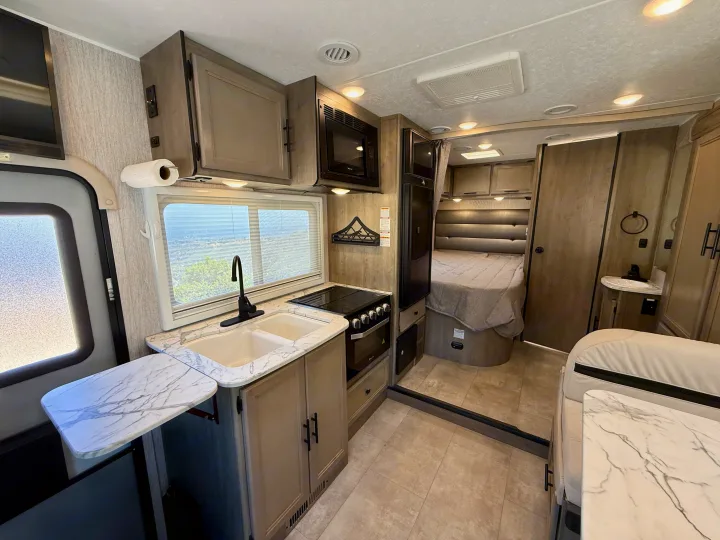 Explore this modern RV rental's well-equipped kitchen with marble-patterned counters, sink, oven, microwave, and a cozy private bedroom.. Coachmen RV Prism Select 24CB 2021