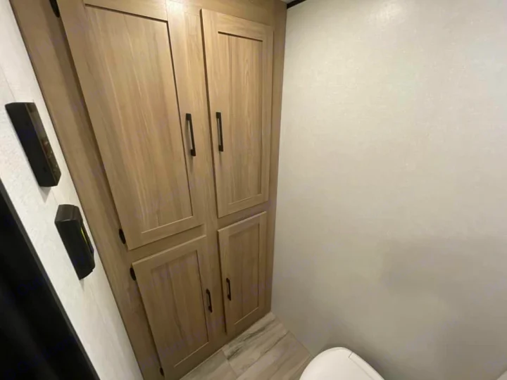 RV rental interior showing light wood cabinets, wall controls, and a portion of the toilet in a compact bathroom.. Keystone RV Coleman 17R 2026