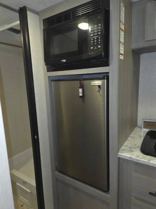 Compact RV rental kitchenette: a black microwave oven over a stainless steel fridge, next to a shower, ideal for travel.. Keystone RV CM17R23 2023