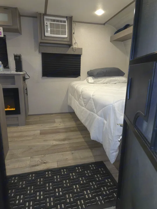 Cozy rv rental bedroom area with bed, AC unit, electric fireplace, and Keurig coffee maker on wood-look floor.. Keystone RV CM17R23 2023