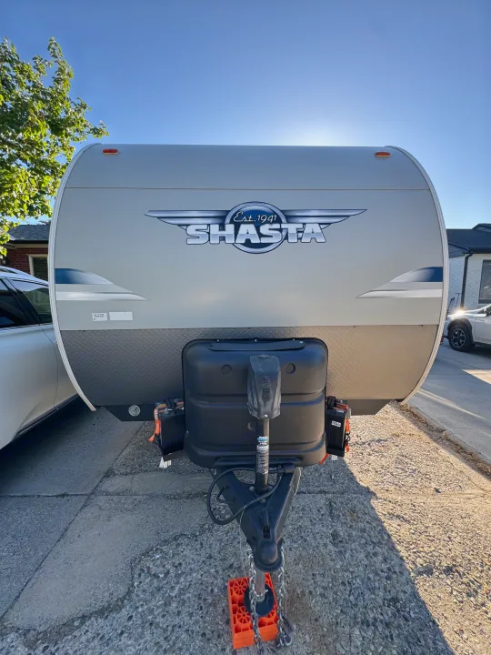 Front of a Shasta travel trailer, ideal for an RV rental. Displays the hitch, covered propane tanks, and bright blue sky.. Forest River Shasta 2021