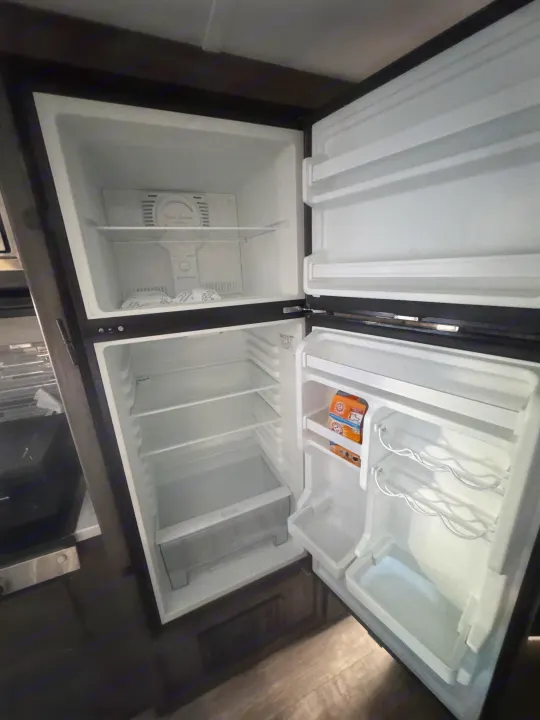 Open, empty refrigerator in an RV rental, showing freezer, shelves, and door storage with baking soda. Ready for your trip!. Forest River Shasta 2021