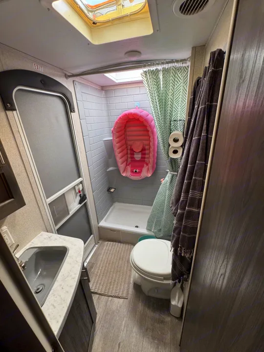 This RV rental's compact bathroom includes a sink, toilet, shower with grey tiles, and a pink infant tub. Perfect for family trips!. Forest River Shasta 2021