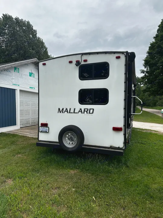 Mallard travel trailer, ideal for rv rental, parked on grass. Features a rear camera, spare tire, and Michigan license plate.. Heartland RVs Mallard 2022