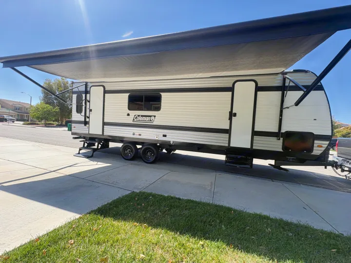 Coleman travel trailer RV rental parked on a driveway with its awning extended under a sunny sky.. Keystone RV Other 2026