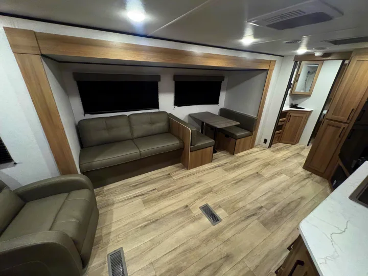 Modern RV rental interior with light wood flooring, grey sofa and dinette, providing a comfortable living space.. Keystone RV Other 2026