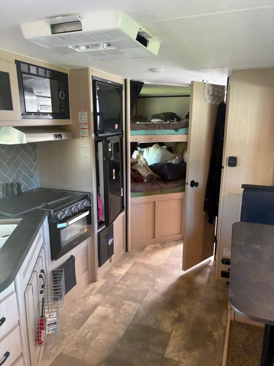 Inside an rv rental: kitchen with stove, microwave, fridge, plus comfortable bunk beds and dinette.. Coachmen Apex 2022