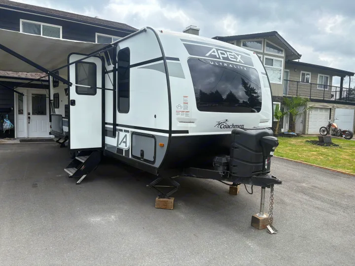 Modern Apex Ultralite travel trailer on a driveway, ready for an RV rental journey with its awning out and steps down.. Coachmen Apex 2022