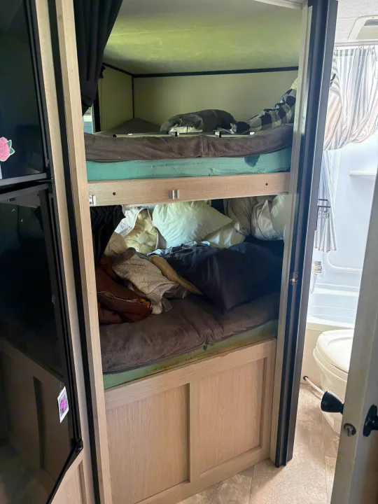 Cozy RV rental interior with bunk beds, blankets, and a glimpse of the small bathroom. Perfect for family adventures.. Coachmen Apex 2022