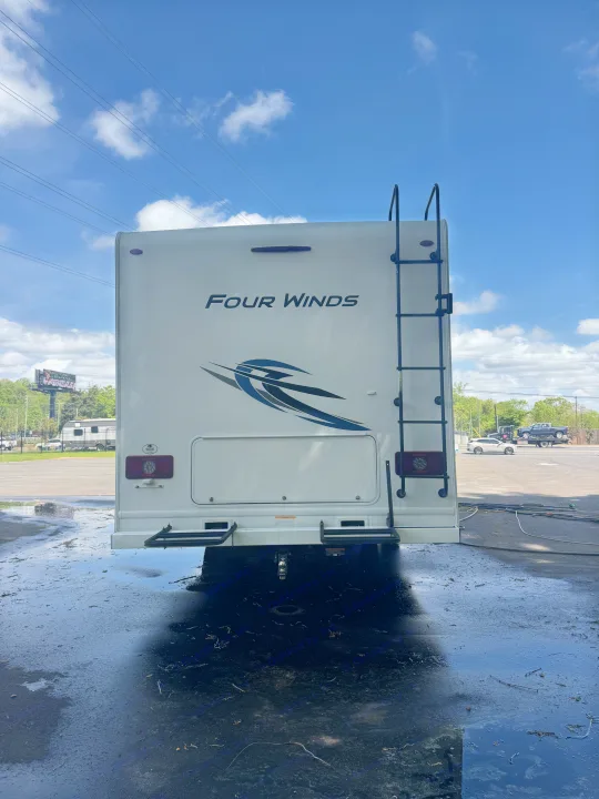 Rear of a white Four Winds RV rental, featuring a ladder and clear tail lights. The wet ground suggests it was recently washed.. Thor Four Winds 2023