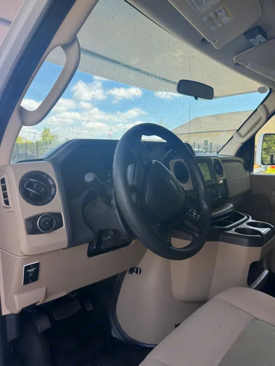Driver's cockpit of an RV rental, featuring the dashboard, steering wheel, and a wet windshield with sky visible beyond.. Thor Four Winds 2023