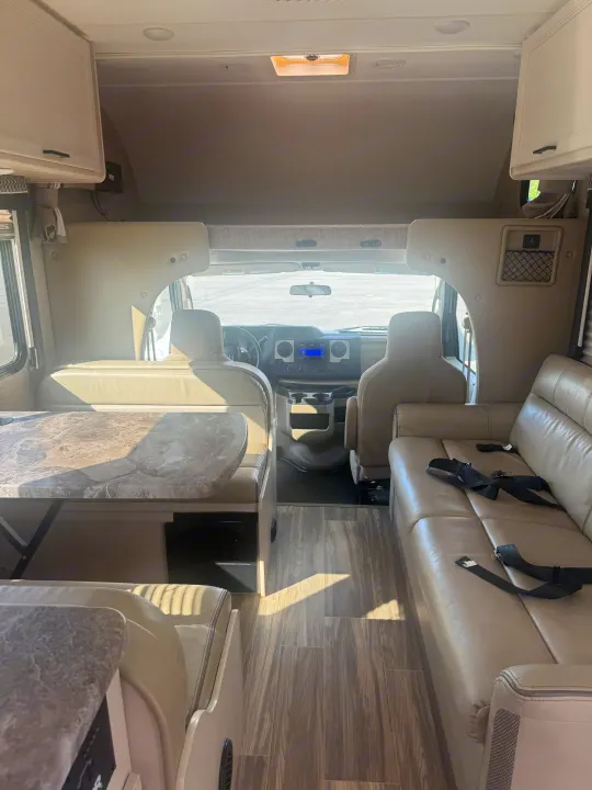 Bright rv rental interior featuring a dinette, lounge seating with seatbelts, and cockpit area. Ready for your travels.. Thor Four Winds 2023