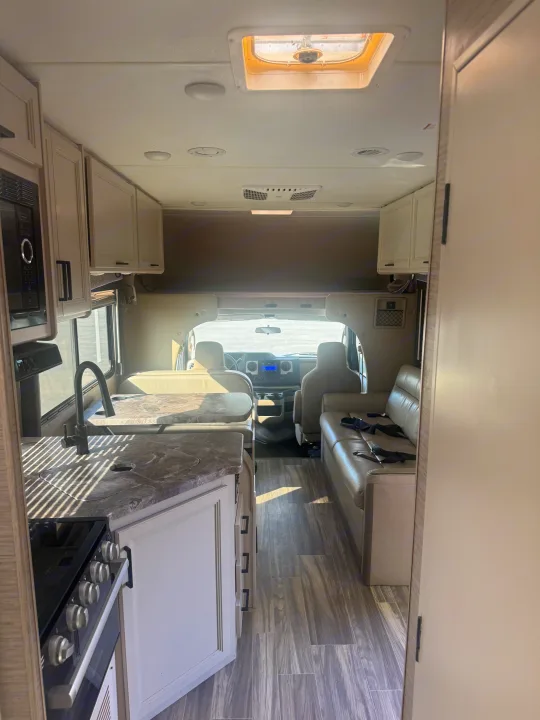 Bright rv rental interior: compact kitchen, dinette, couch with seatbelts, & front cockpit.. Thor Four Winds 2023