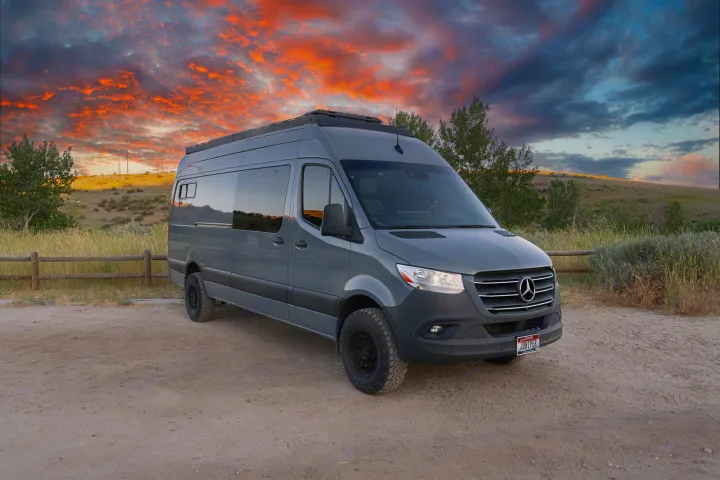 Grey Mercedes Sprinter van, an ideal RV rental, parked on dirt near a fence under a vibrant sunset sky.. MERCEDES-BENZ SPRINTER 2500 170 WB 2022