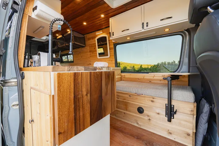 Cozy RV rental interior: customized wooden kitchen, faucet, and comfy window bench with a view. Ideal for mobile adventures.. MERCEDES-BENZ SPRINTER 2500 170 WB 2022