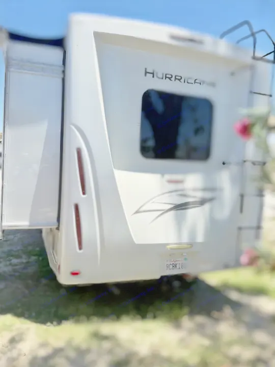 White Hurricane RV rental parked outdoors. Rear view shows an extended slide-out, ladder, and California license plate.. Thor Hurricane 2024