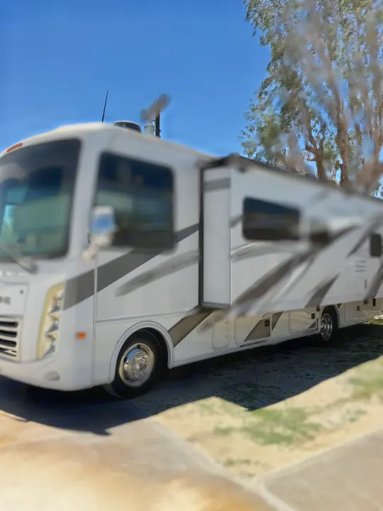 Bright white & gray motorhome with an extended awning, parked outside. Perfect for your next rv rental getaway.. Thor Hurricane 2024