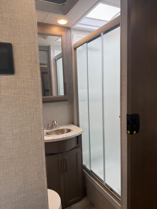 Compact RV rental bathroom featuring a sink vanity, a shower with frosted sliding doors, and a toilet.. Thor Hurricane 2024