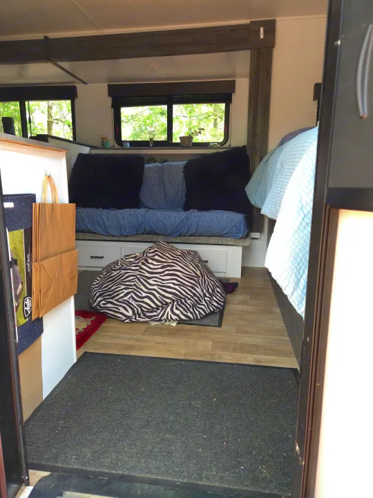 Cozy rv rental interior, showing a blue couch, zebra beanbag on the floor, and a bed with light blue bedding from the entrance.. Keystone RV Hideout 2022