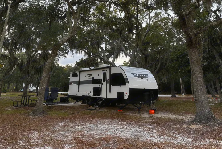 An RV rental (travel trailer) at a mossy campground with a picnic table & chairs, ready for adventure.. Forest River Wildwood X-Lite Platinum 2024