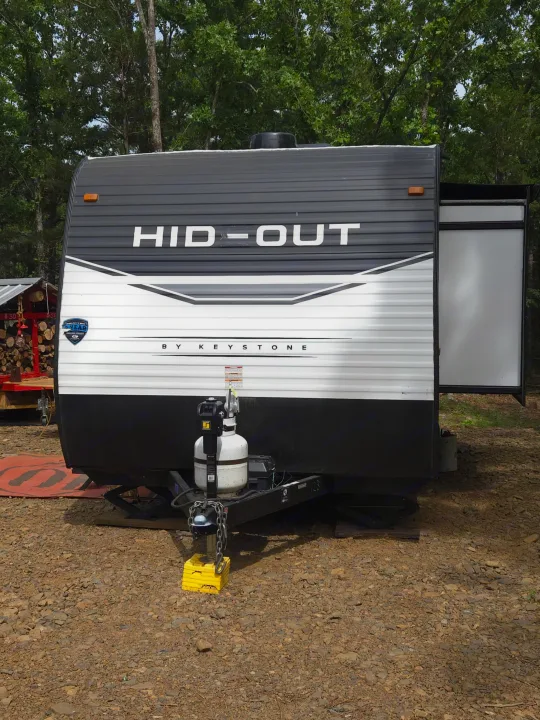 Front view of a HID-OUT by Keystone travel trailer, ideal for an RV rental, parked on gravel with an extended slide-out.. Keystone RV Hideout 2022