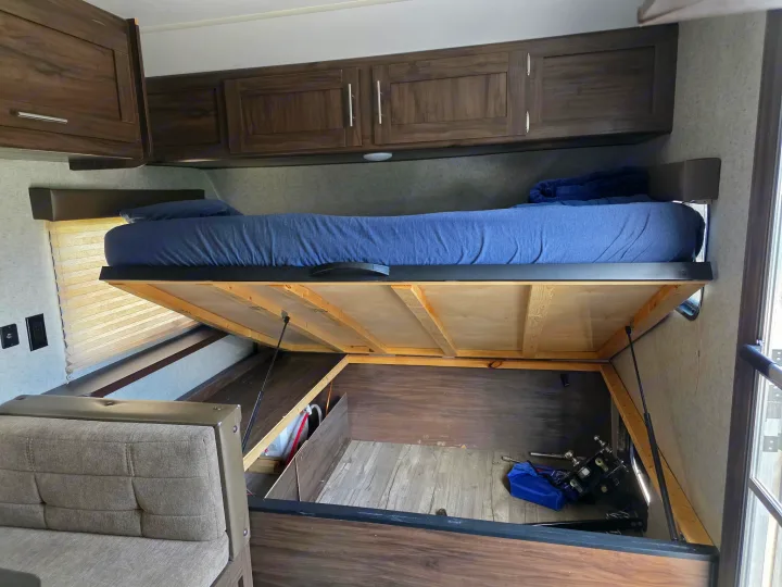 This rv rental features a lift-up bed revealing ample under-bed storage, with additional overhead cabinets visible.. Forest River Cherokee Wolf Pup 2018