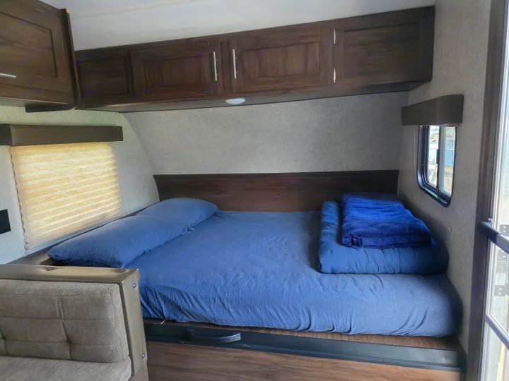 Inside this RV rental, a comfy sleeping area features blue bedding, overhead cabinets, and a window for natural light.. Forest River Cherokee Wolf Pup 2018