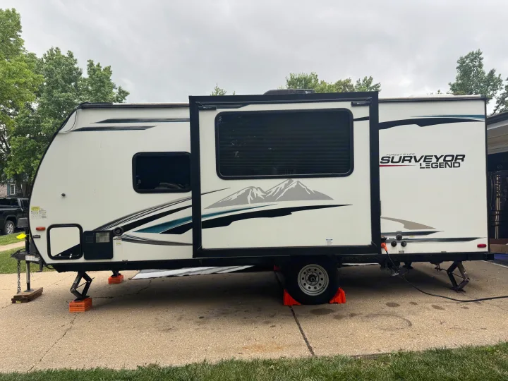 White Surveyor Legend rv rental travel trailer with an extended slide-out, leveled on a driveway with orange blocks.. Forest River Surveyor Legend 2021