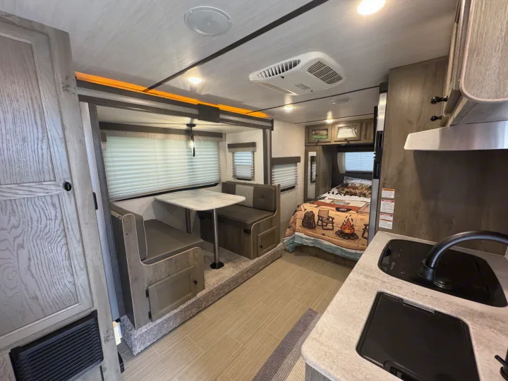 RV rental interior: dinette, compact kitchen with sink/stove, and a cozy bedroom with camping-themed bedding. Modern, functional design.. Forest River Surveyor Legend 2021