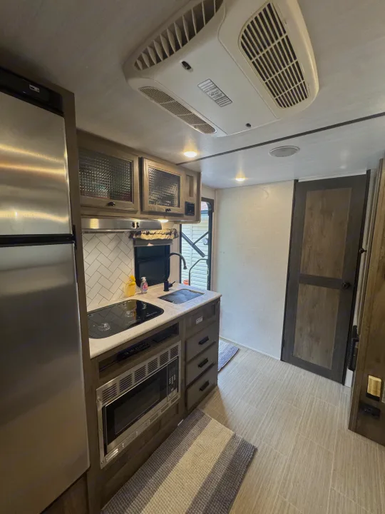 Experience comfort in this RV rental's modern kitchen: fridge, cooktop, microwave, stylish cabinets, and bright, clean design.. Forest River Surveyor Legend 2021