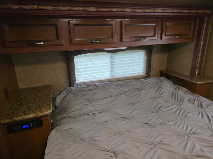 RV rental bedroom with a grey bed, overhead storage cabinets, window with blinds, and nightstands, one featuring a control panel.. Thor Four Winds 2015