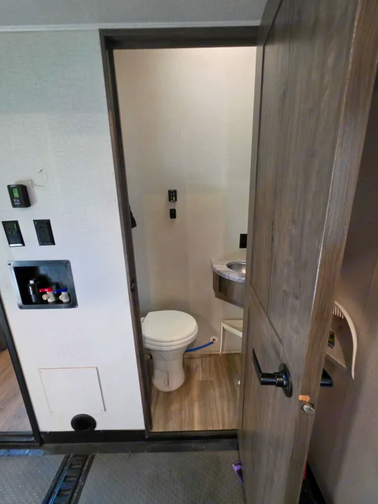 Inside an RV rental: a compact bathroom with toilet and sink. Nearby wall shows utility hookups for appliances.. Alliance RV Valor 40V13 2021
