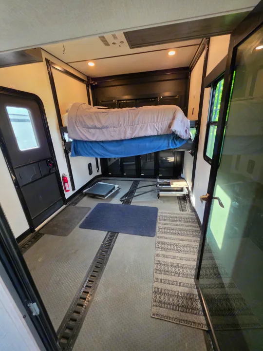 RV rental toy hauler interior with a suspended bed, cargo tracks, side door, and steps. Versatile camper space.. Alliance RV Valor 40V13 2021