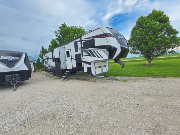 Two modern RVs, a large black and white fifth-wheel and a smaller travel trailer, parked on a gravel lot, perfect for an RV rental.. Alliance RV Valor 40V13 2021