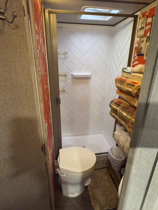 Inside a compact RV rental bathroom: toilet, shower with herringbone tiles, and shelving with rolled towels.. Forest River Salem FSX 2025