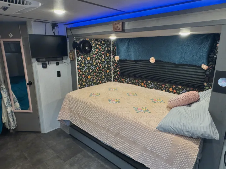 Cozy rv rental bedroom: floral-patterned wallpaper, quilt-covered bed, TV, fan, and blue accent lighting create a comfortable interior.. Forest River Salem FSX 2025