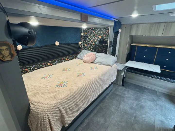 Cozy RV rental bedroom features a floral-decorated bed with a textured comforter, blue LED lights, and a compact dinette.. Forest River Salem FSX 2025
