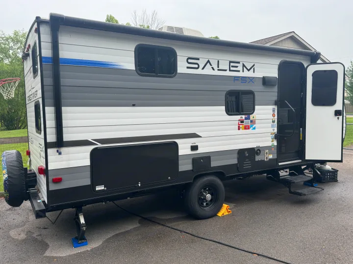 This Salem FSX travel trailer, a compact RV rental, is set up with leveling jacks and wheel chocks, ready for adventure.. Forest River Salem FSX 2025