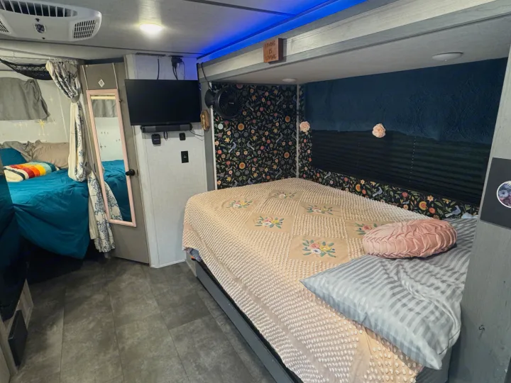 Cozy RV rental bedroom showcasing a large bed, TV, mirror, and bunk. Features unique floral wallpaper, blue accent lights, and an AC unit.. Forest River Salem FSX 2025