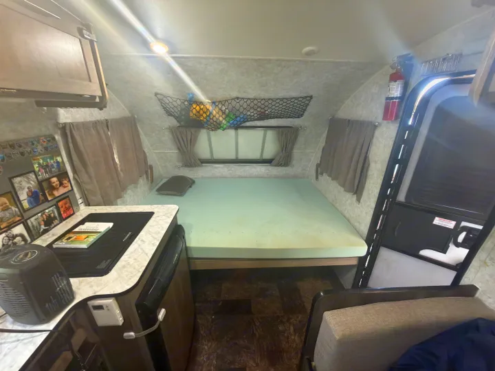 This RV rental interior features a cozy bed, compact kitchen counter with family photos, and an entry door.. Prolite Lounge 2021