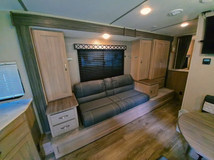 Cozy rv rental living space featuring a gray sofa bed, light wood cabinetry, window blinds, and modern decor.. Coachmen Freedom Express 2021