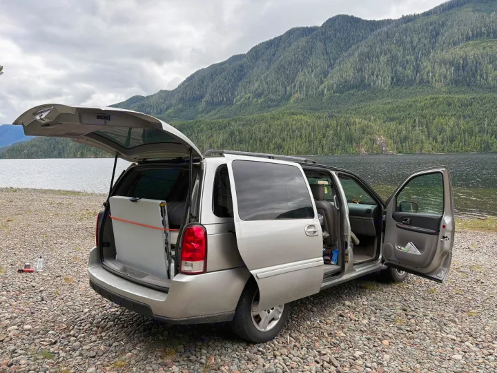 Minivan parked lakeside with open trunk & gear, perfect for camping. A smart alternative to an RV rental for adventure.. chevy uplander 2006