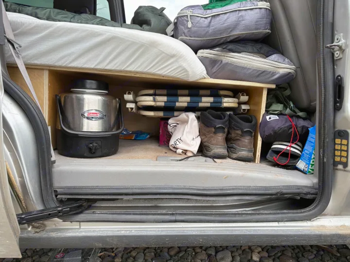 Organized rv rental van setup: Sleeping platform, custom storage with Coleman jug, hiking boots, chairs, and bags for adventure.. chevy uplander 2006