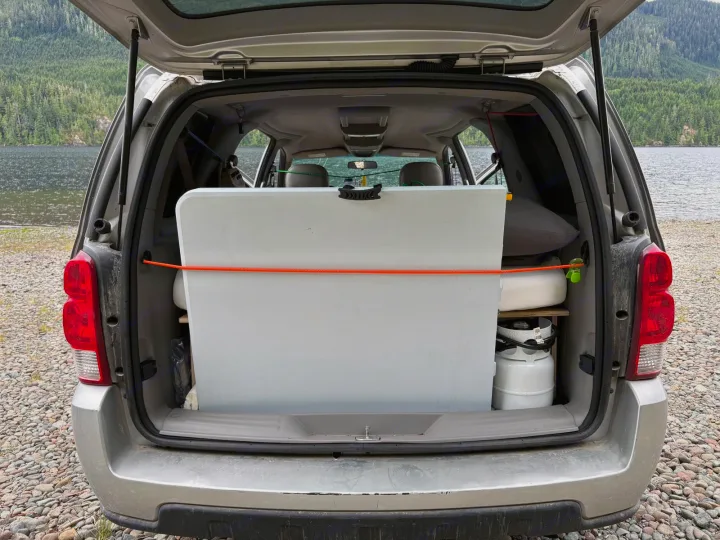 RV rental SUV's organized trunk: a white folding table, propane tank, and camping supplies, ready for a lakefront adventure.. chevy uplander 2006
