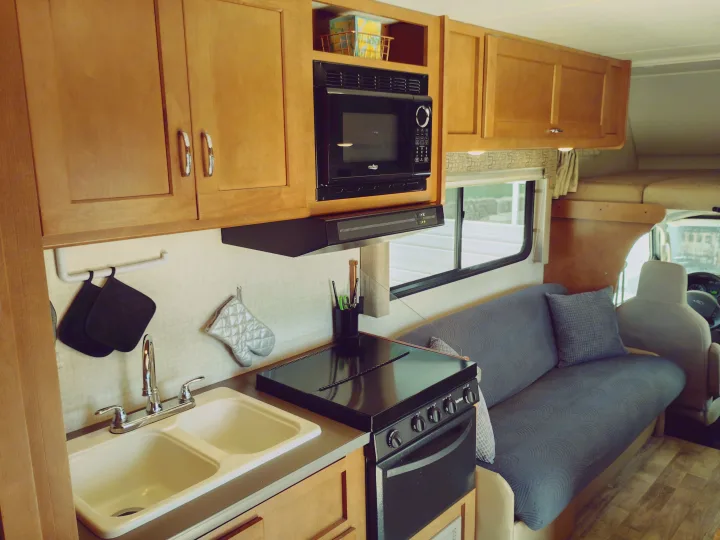 Inside an RV rental: a compact kitchen with wood cabinets, sink, microwave, stove, and an inviting sofa for your adventures.. Winnebago Minnie Winnie 2017